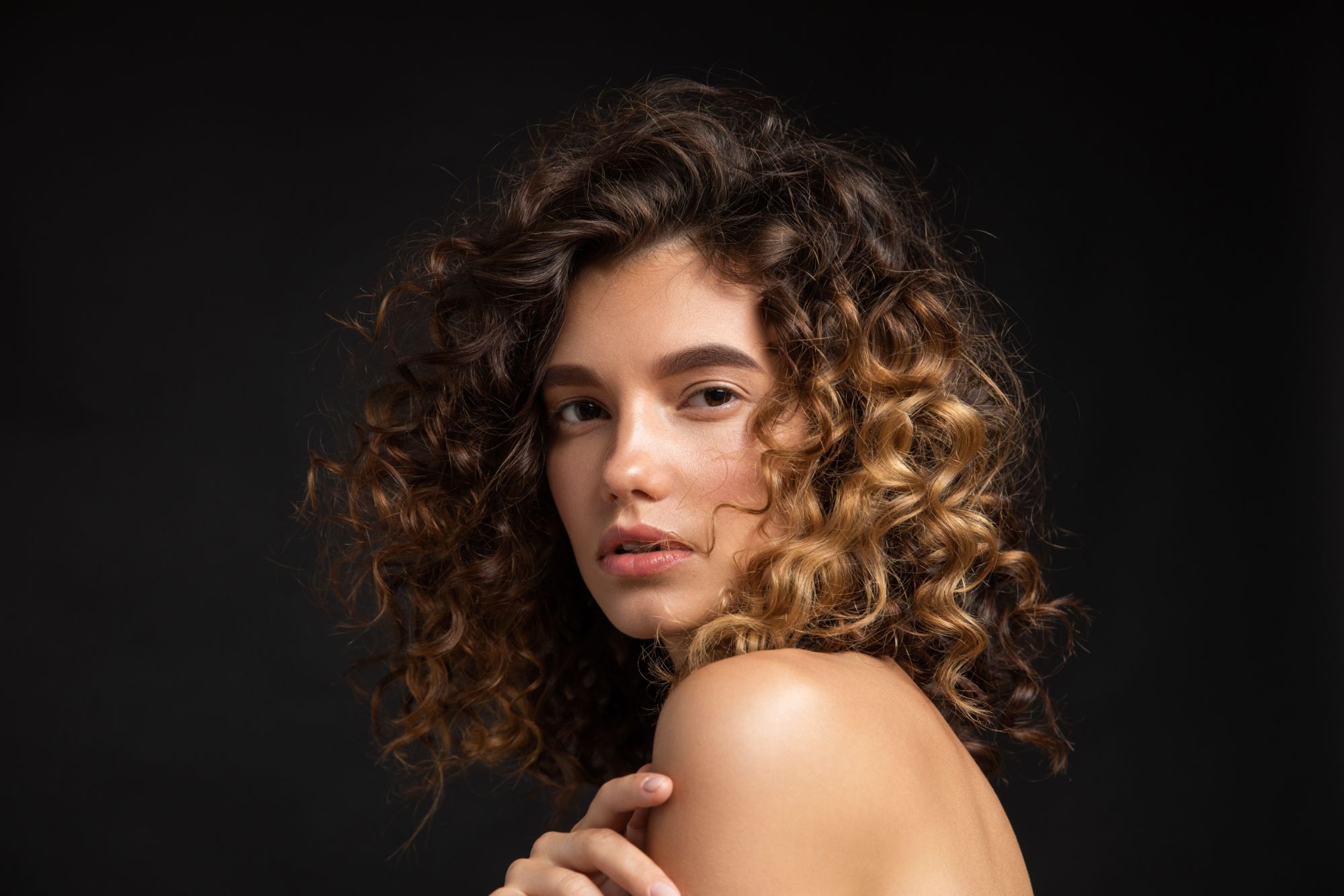 Woman with curly hair against black background.