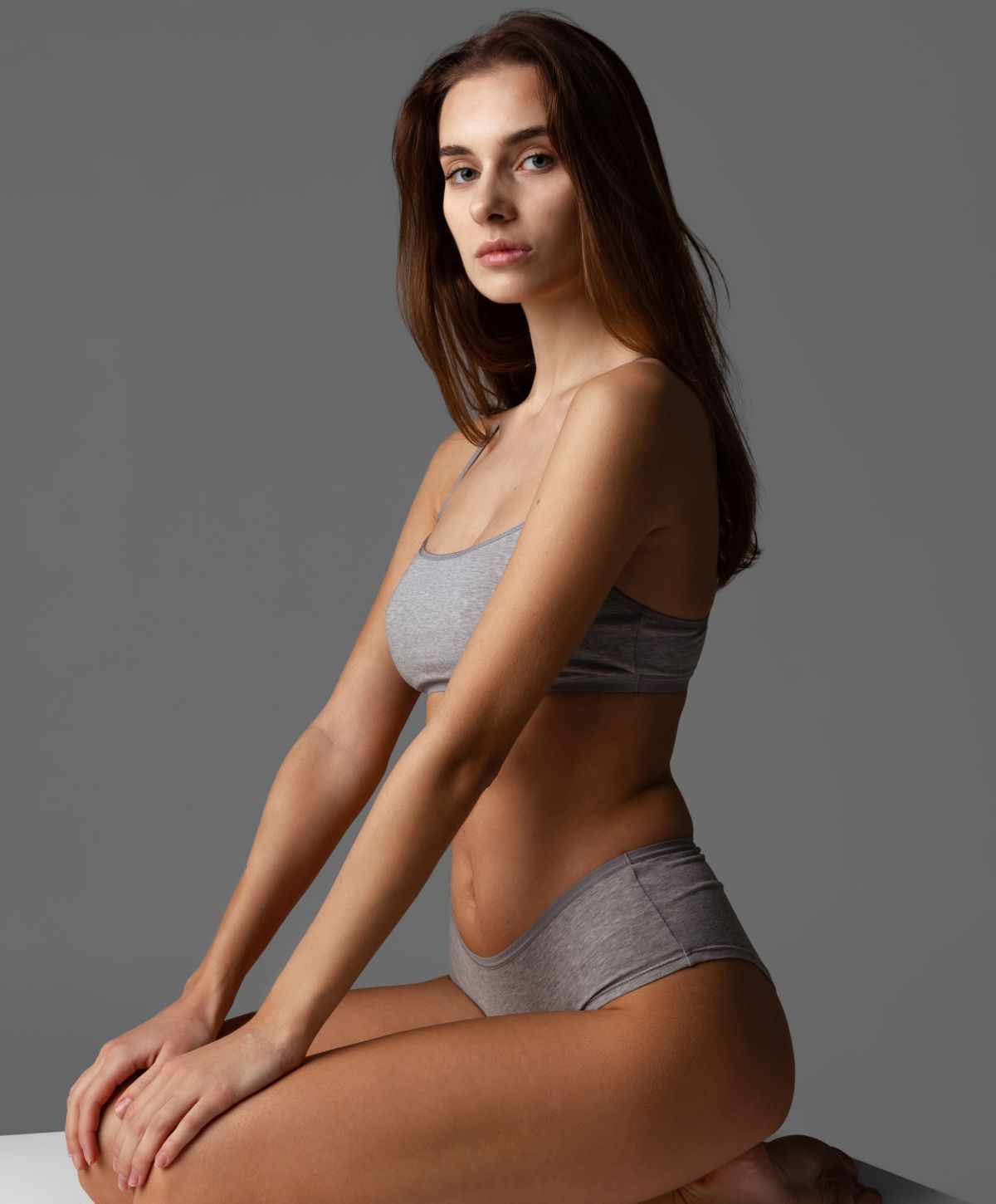 Denver tummy tuck model in black bra gazing out window.