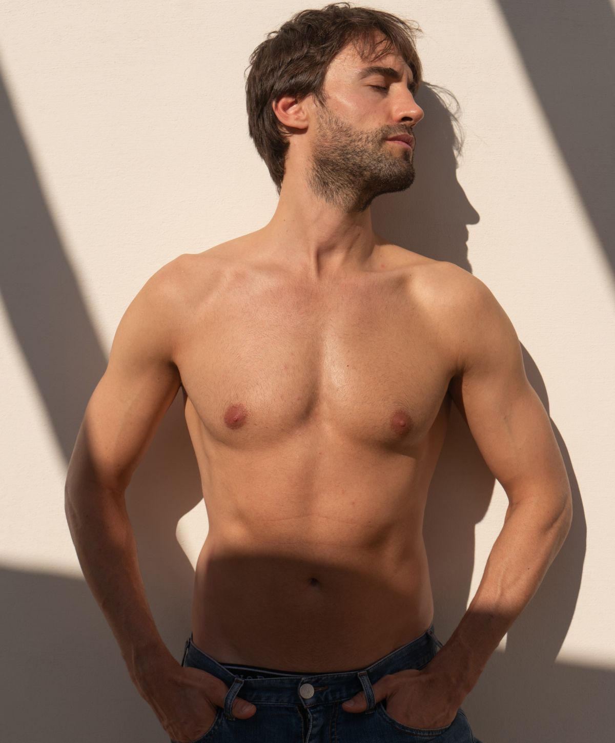 Shirtless man leaning against a wall.