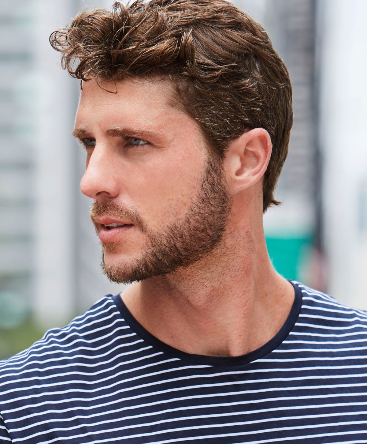 Man with stylish hair wearing striped shirt outdoors.