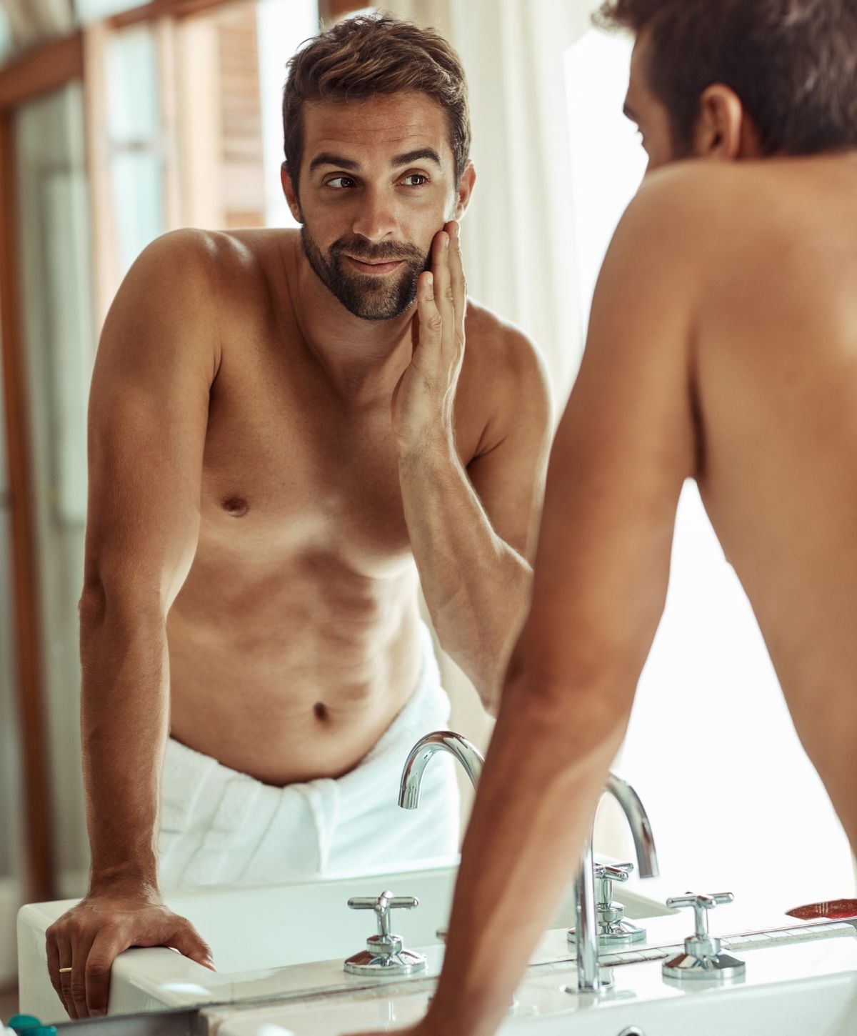 Man grooming in front of a bathroom mirror.