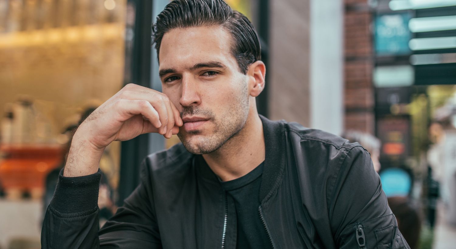 Denver male facial fillers model thoughtfully resting chin on hand outdoors.