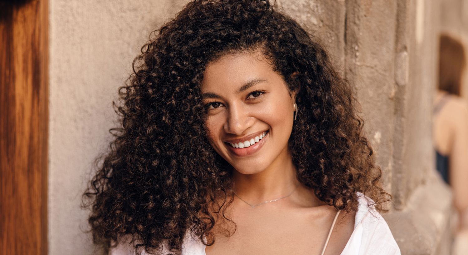 Smiling Denver microneedling boosters model with curly hair outdoors.